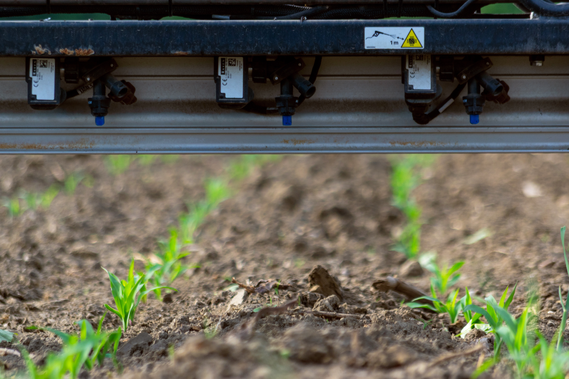 RAVEN individual nozzle valve system mounted on a spray boom above young corn seedlings